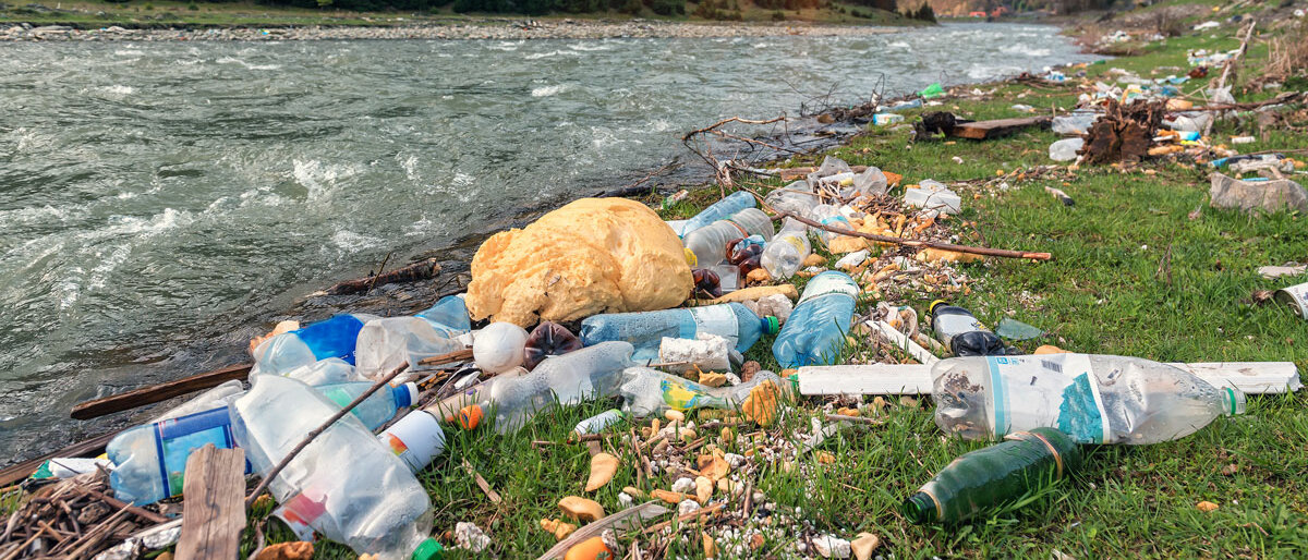 Ein Fluss in den Bergen, am Ufer ein Haufen Plastikmüll