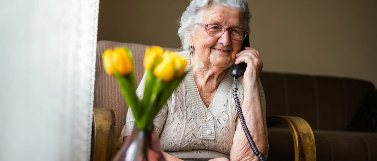 Glückliche Seniorin, die im Wohnzimmer telefoniert.