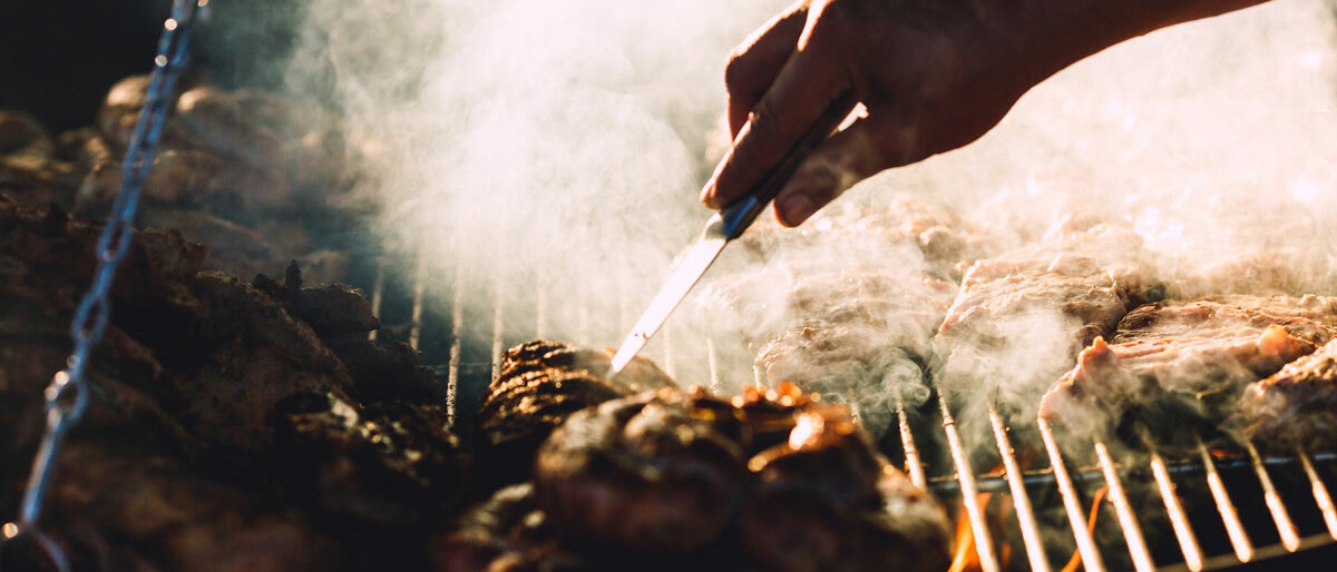 eine Hand wendet Fleisch auf einem rauchigen Grillrost