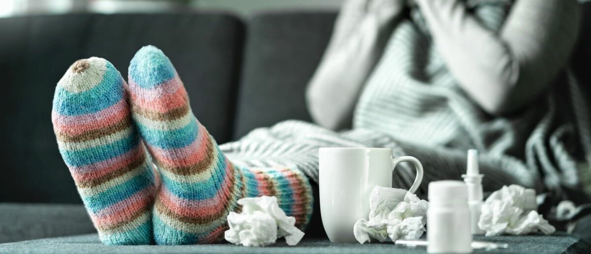 Grippe Eine Frau sitzt auf der Couch und putzt sich die Nase.