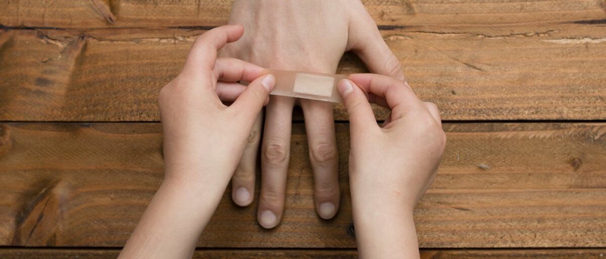 Nahaufnahme: Kinderhände bringen ein Pflaster auf einer erwachsenen Hand an.