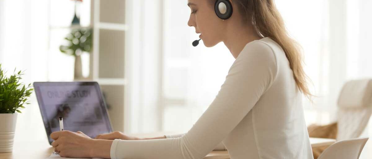 Eine junge Frau sitzt zu Hause vor ihrem Laptop, trägt ein Headset und nimmt an einem Online-Kurs teil.