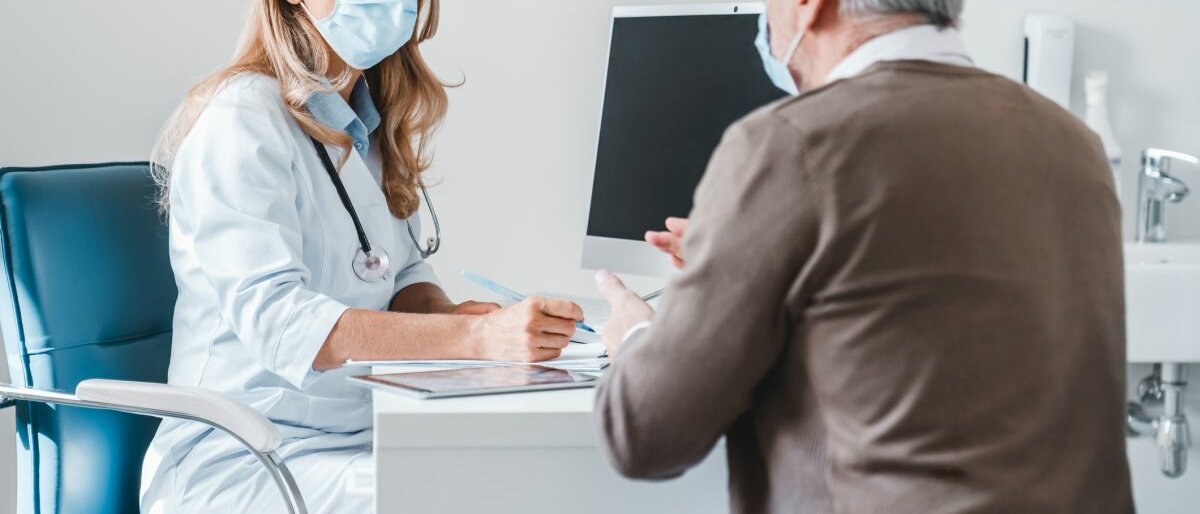 Eine Ärztin trägt während des Gesprächs mit einem Patienten in einer Arztpraxis eine Schutzmaske.