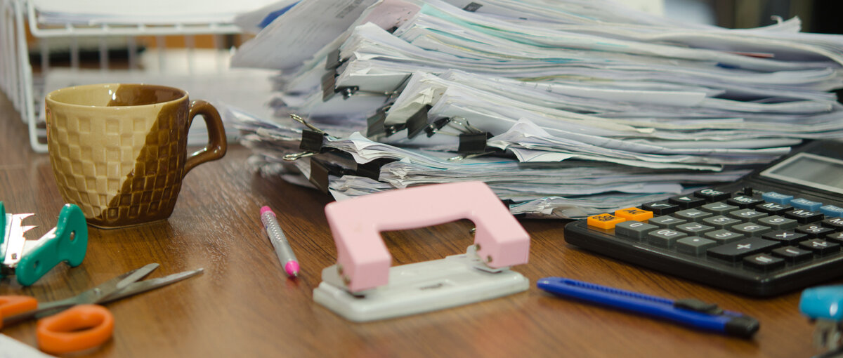 Auf einem Schreibtisch türmen sich Papiere, die mit Papierklammern sortiert wurden.