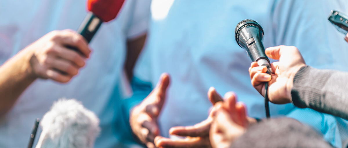 viele Mikrofone richten sich auf eine Person im Hintergrund